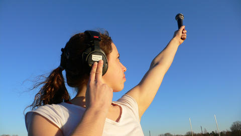 Photo of girl wearing headphones directing microphone to the sky